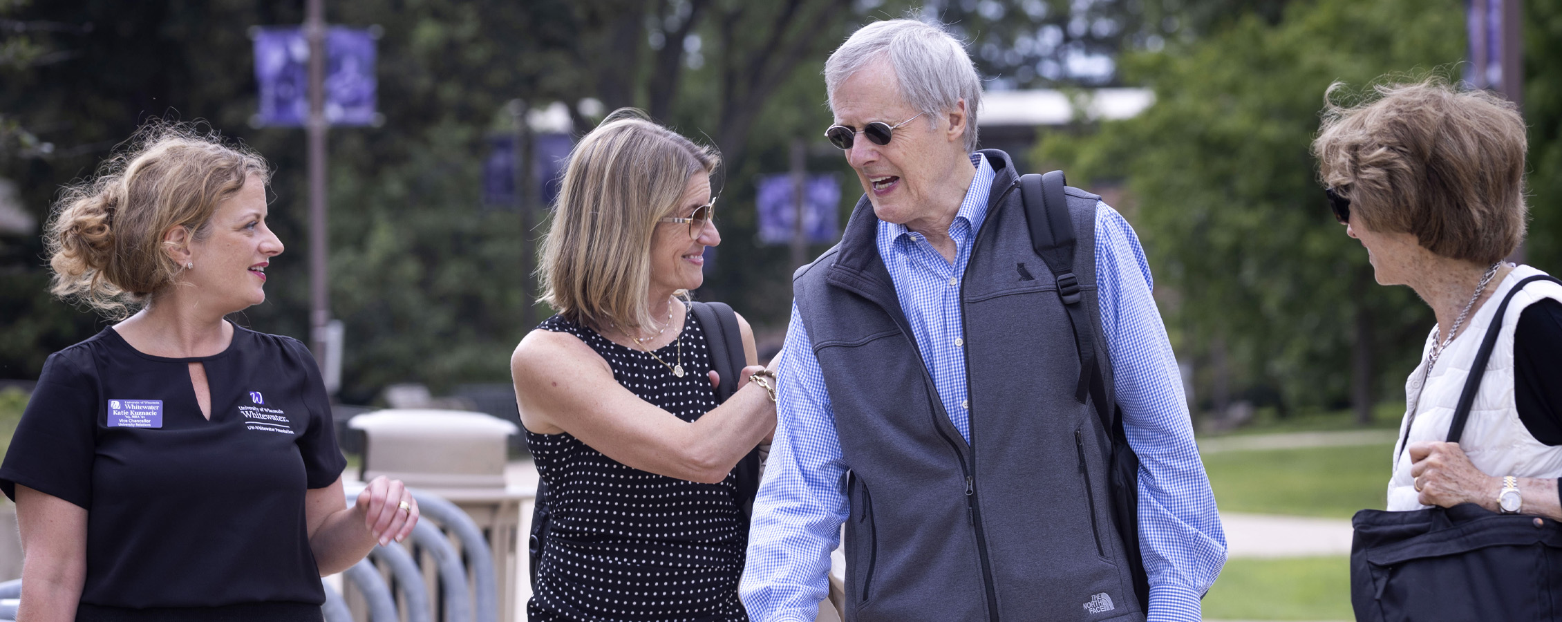 A group of four people walk and smile together on the UW-Whitewater campus.