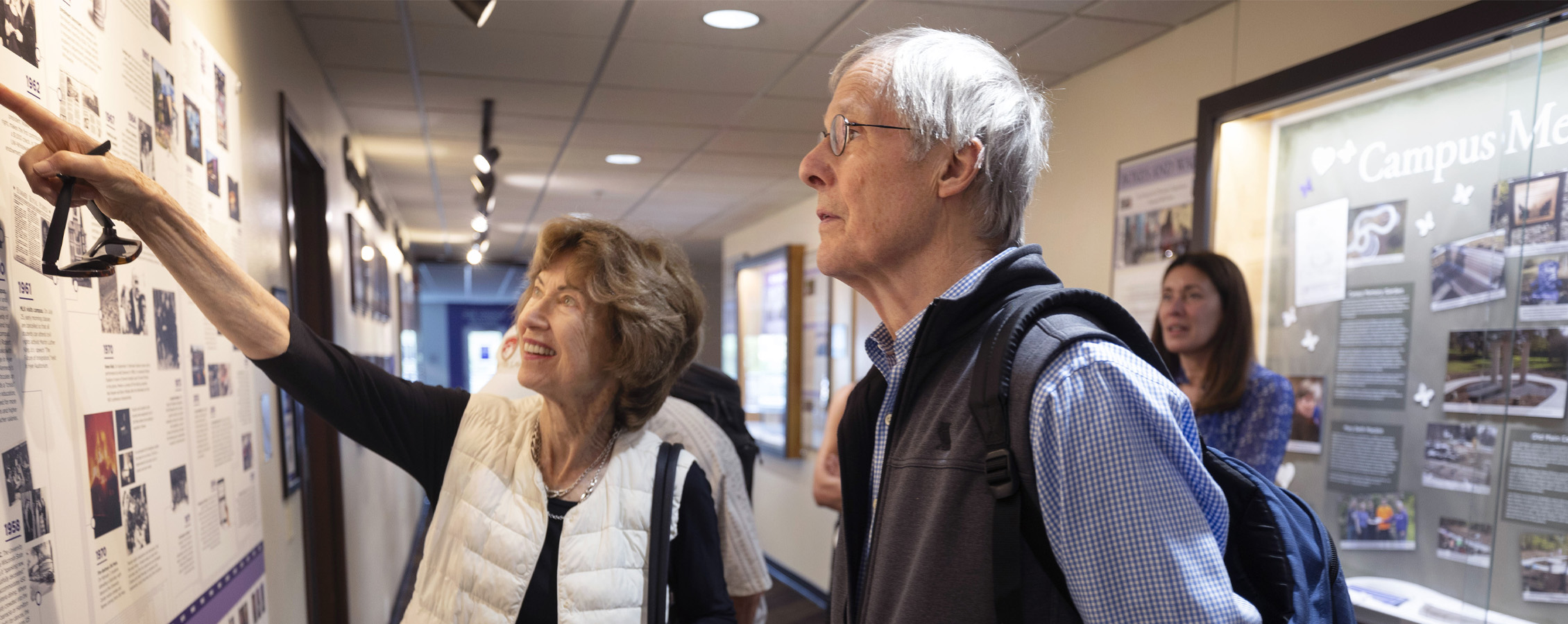 Two people standing together point at a poster on the wall.