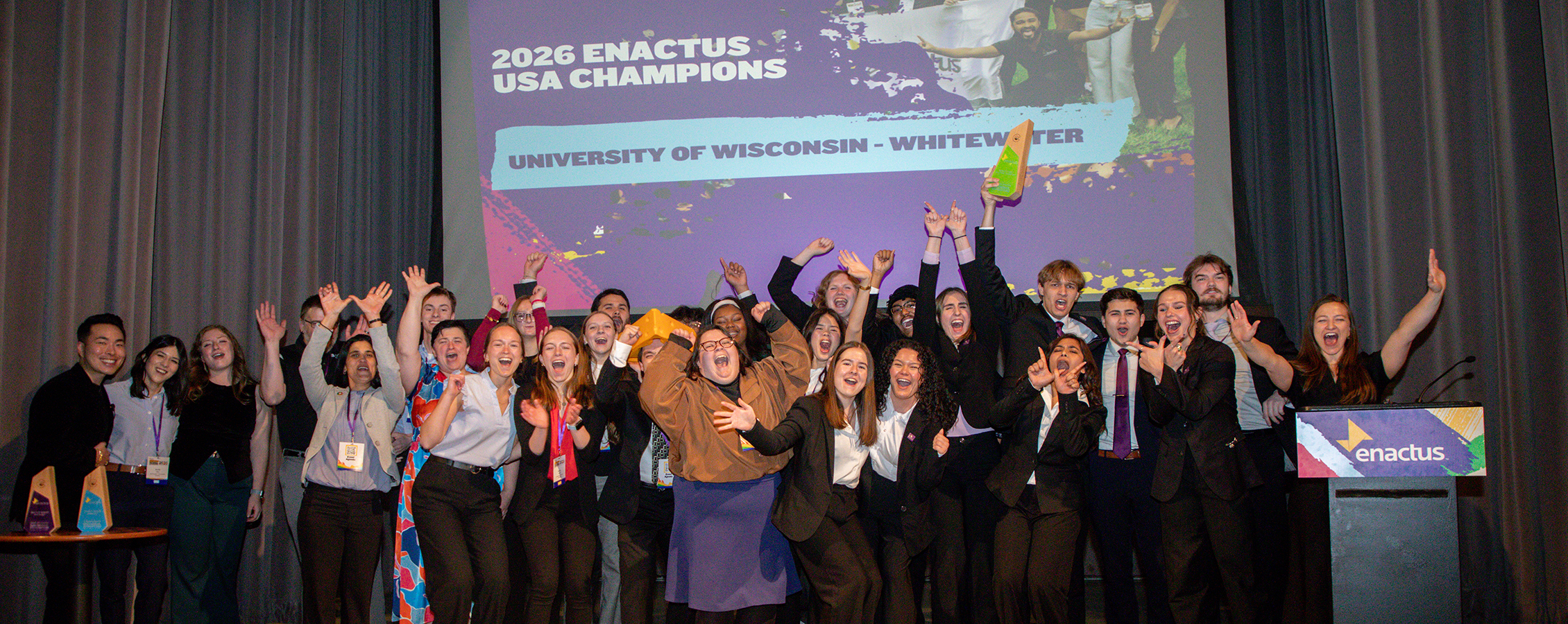 A group of people stand together with their arms raised in celebration.