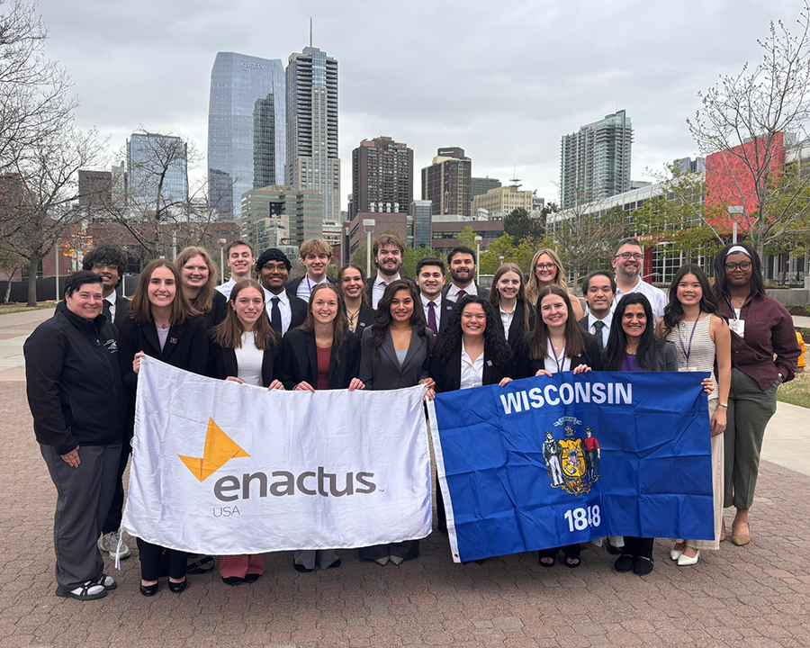 The Enactus team stands together in front of a city skyline holding an Enactus flag and a Wisconsin flag.