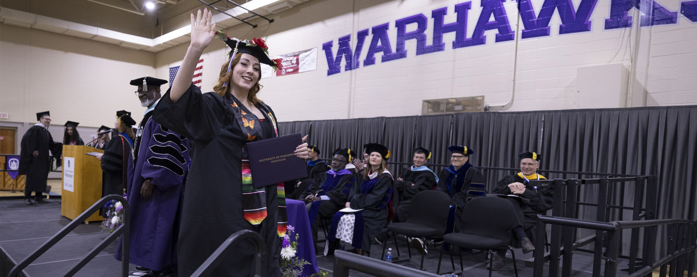 A graduate waves as they walk across the stage at the commencement ceremony.