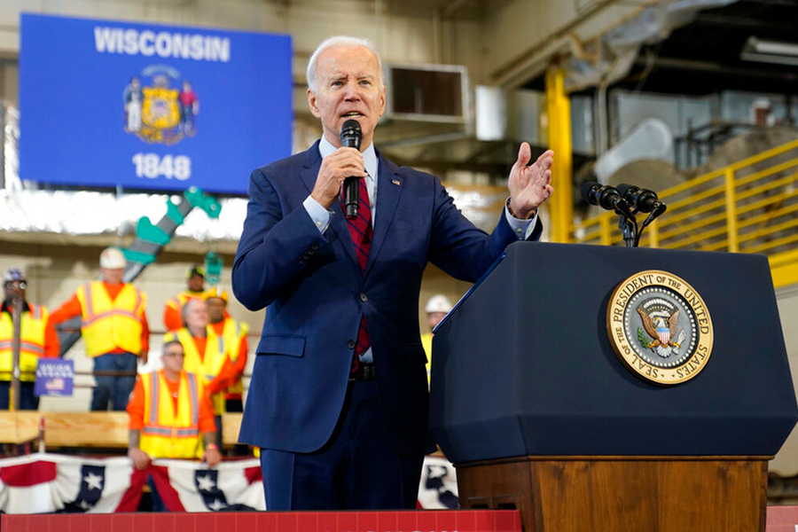 president joe biden speaks to a crowd of people from behind a podium in front of the wisconsin state flag