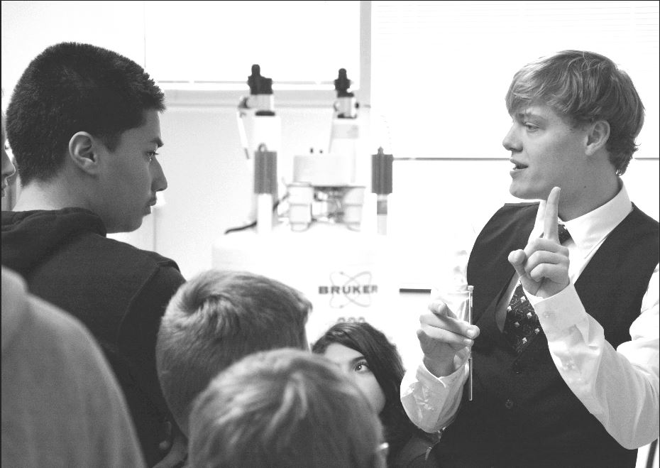 A presenter speaks to a group of students in front of a spectrometer