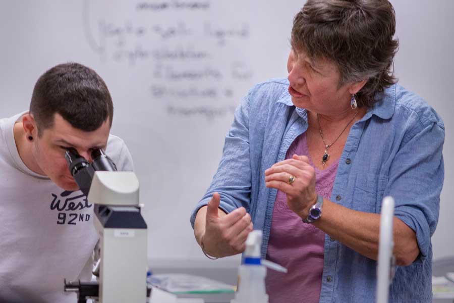 A professor and student examining a microscope