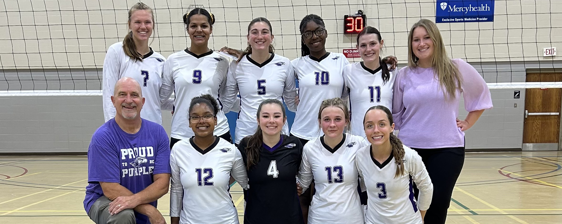 Volleyball players stand on the court with their arms around each other as they pose for a photo.