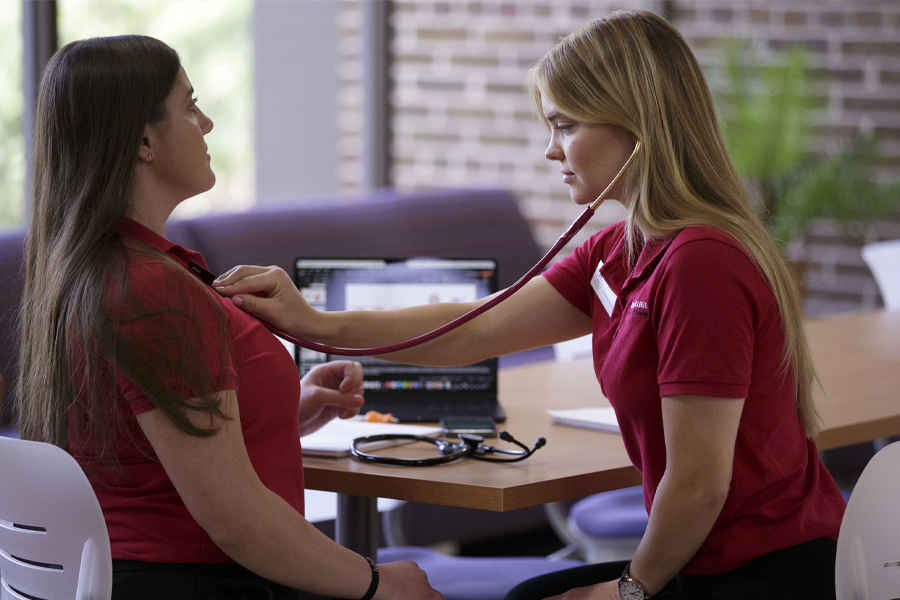 A student uses a stethoscope to listen to another student's chest.