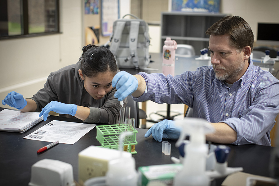 A student and faculty member work in a lab with vials and test tubes.