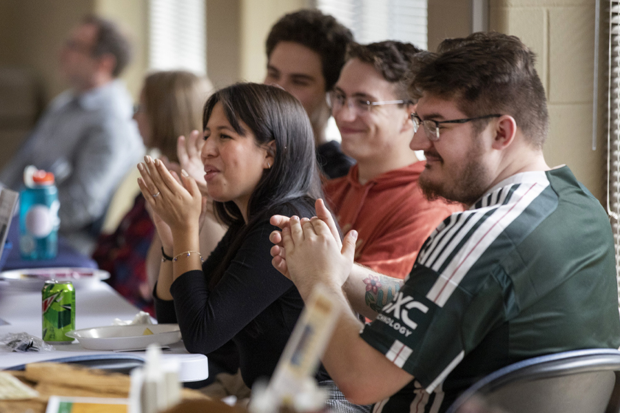 People sitting at table clap and smile.