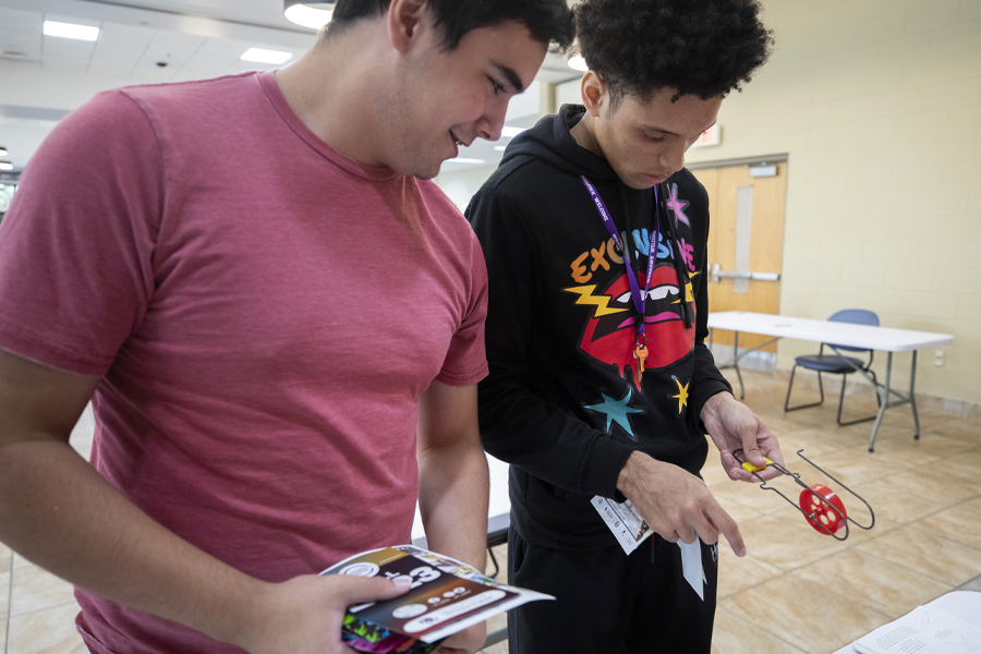 Two students look at a red device that uses magnets to regulate speed at the Engineering Club table.