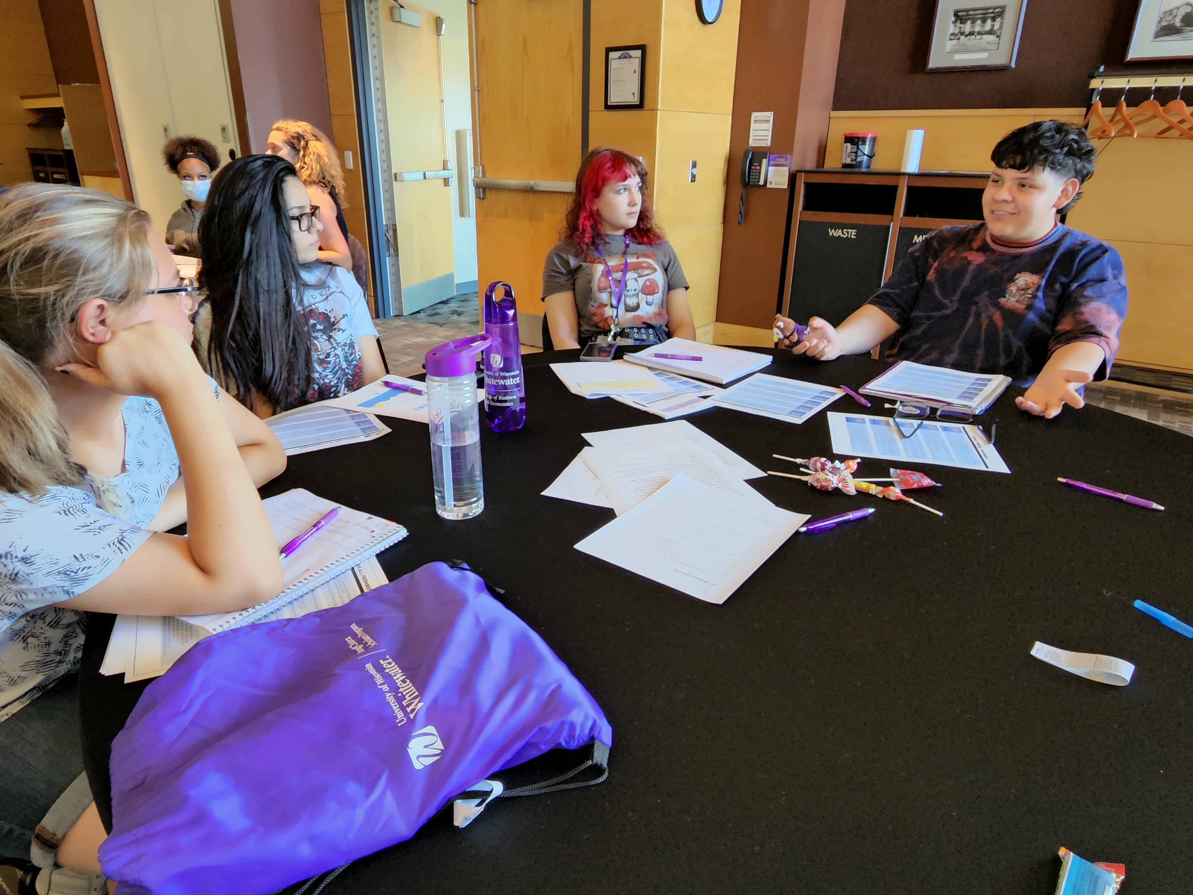 Students a faculty member sit in a circle with papers on the table.