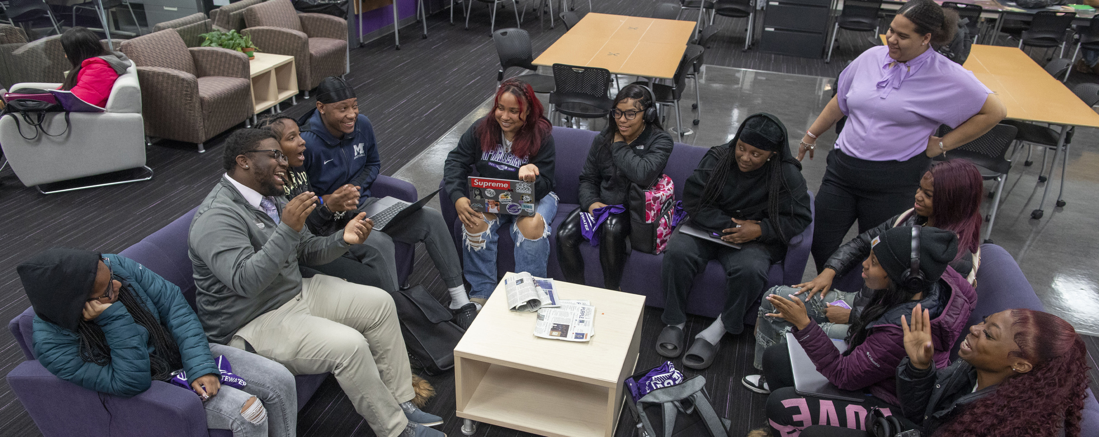 A group of students sit and converse together in comfy chairs. 