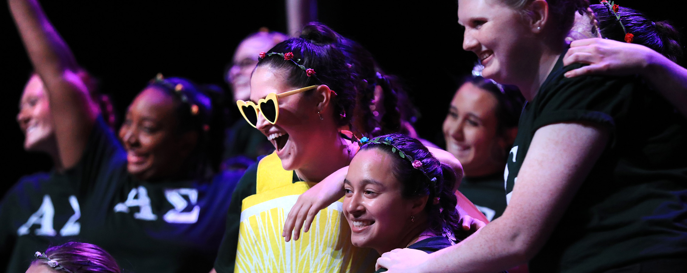 Group of sorority members at a talent show wearing their sorority t-shirts with one member wearing a yellow shirt and yellow sunglasses.