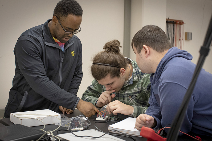 Three students work together in a lab classroom and work on building wire circuits.