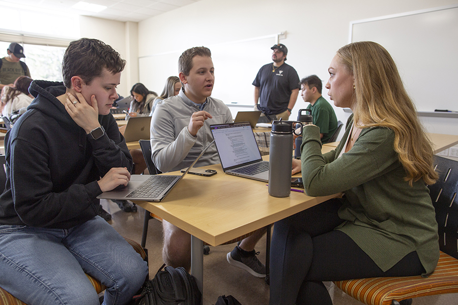 Students smile and laugh together in a classroom with bright windows in the back of the room.