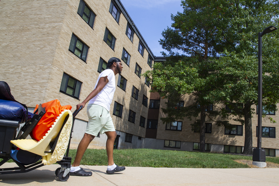 A student pulls a cart full of their belongings in front of a brick building.