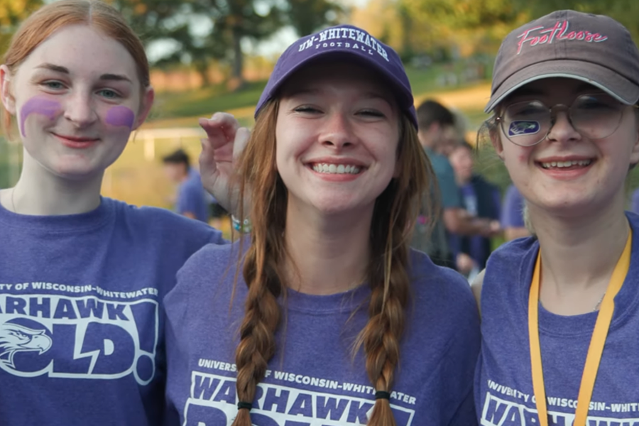 Three students in purple shirts smile at the camera.