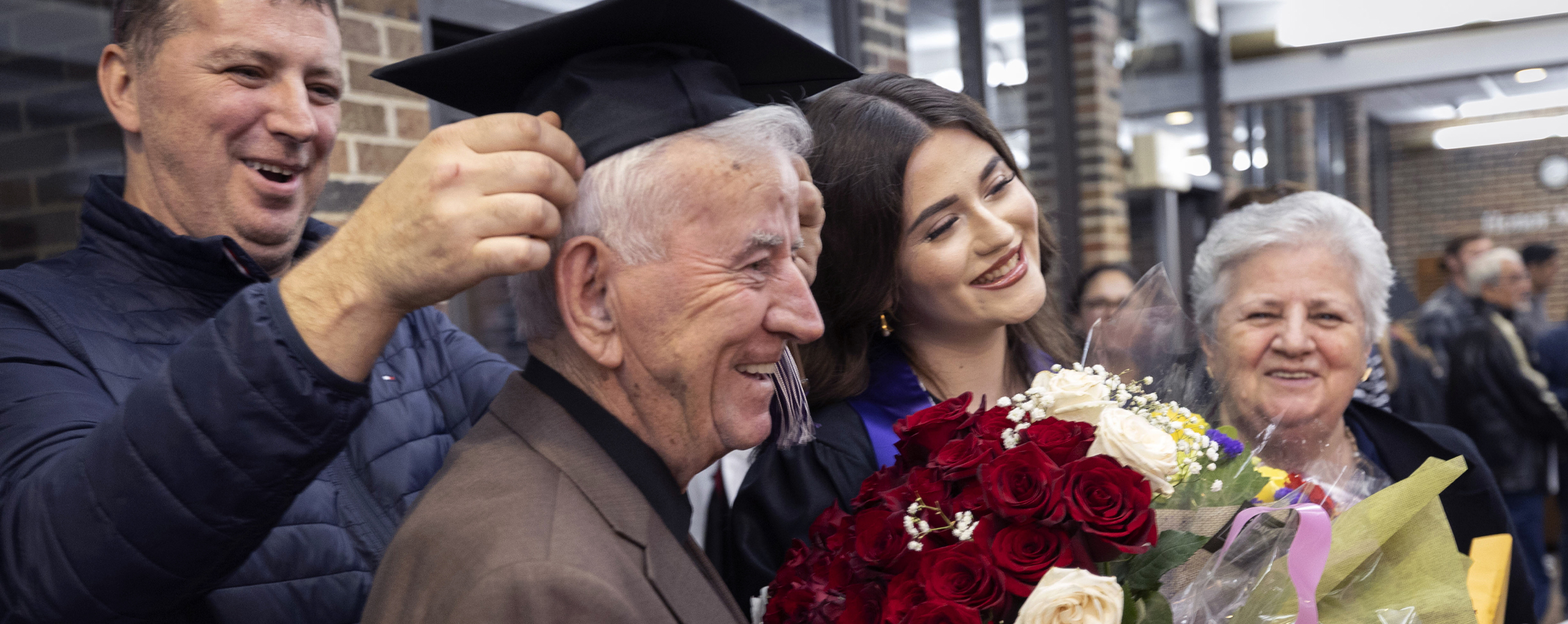 A graduate holding red roses stands with a senior couple.