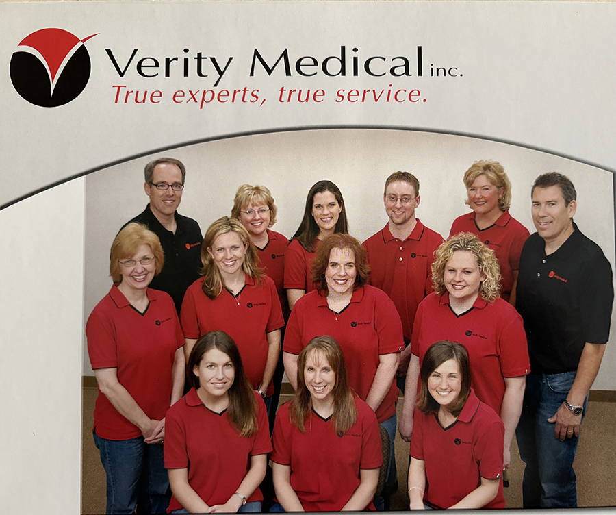 A group of people pose for a photo in front of a red sign that says Verity Medical.